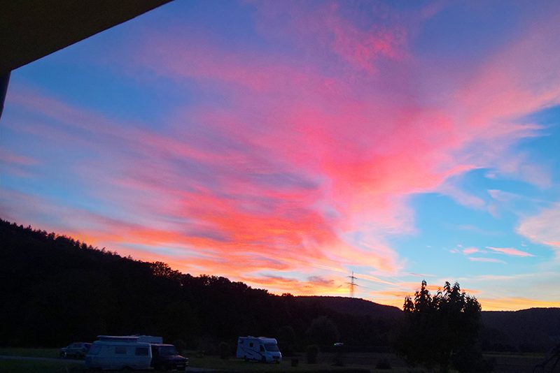 Wohnmobile auf dem Campingplatz Cimbria vor einem rosa-orangen Abendhimmel